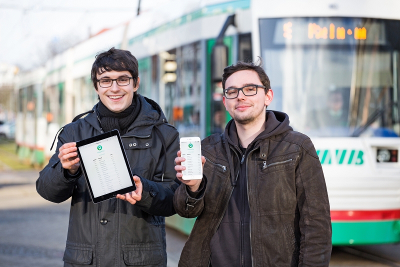 Rosario Raulin und Johannes Filter zeigen Smartphones mit ihrer App vor einer Strassenbahn